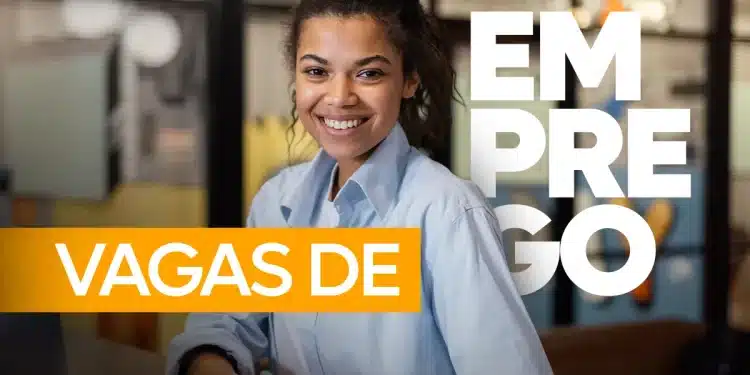 Jovem mulher negra sorridente com cabelos cacheados presos, vestindo camisa social azul claro, sentada em um escritório. Sobre a imagem, há o texto em destaque "VAGAS DE EMPREGO" em cores branco e laranja.