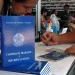 Mulher preenche formulário ao lado de Carteira de Trabalho em mesa de atendimento