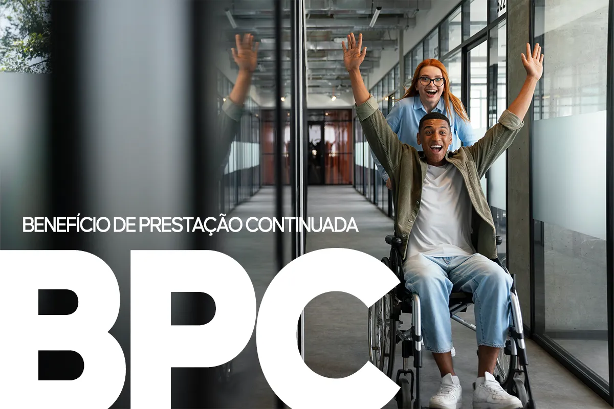 Homem em cadeira de rodas ergue os braços sorrindo com mulher atrás em corredor de escritório moderno