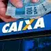 Trabalhador segurando notas de cem reais em frente à agência da Caixa sobre prazo final para saque de até R$ 6.220 pelo aplicativo.