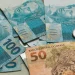 Pagamento do INSS em fevereiro com notas de real e moedas representando benefício de R$ 8.475,55.