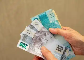 Notas de 200 reais em mãos, representando a nova rodada de pagamentos do INSS, com foco no valor e a distribuição dos benefícios.