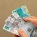 Notas de 200 reais em mãos, representando a nova rodada de pagamentos do INSS, com foco no valor e a distribuição dos benefícios.