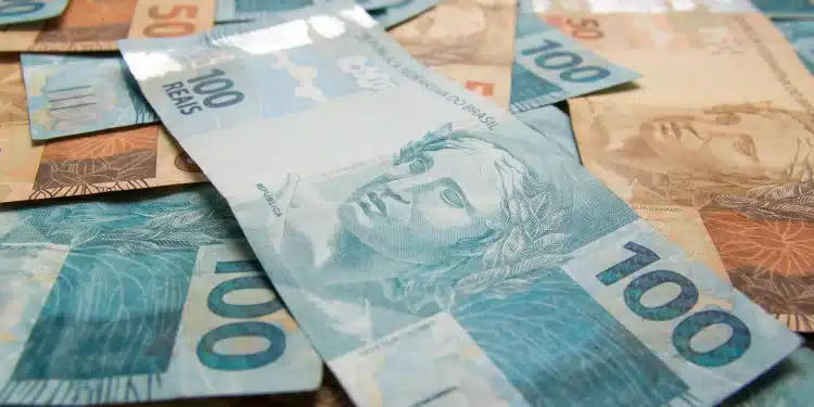 Notas de dinheiro brasileira, com destaque para a cédula de R$ 100 e R$ 50, representando valores de auxílio financeiro para o programa Pé-de-Meia 2026.