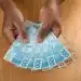 Notas de cem e cinquenta reais sendo seguradas com as mãos, representando o pagamento do INSS disponível em fevereiro de 2026.