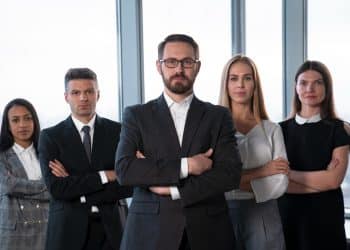 Grupo de cinco executivos de braços cruzados em escritório representando profissões CLT bem remuneradas no Brasil.