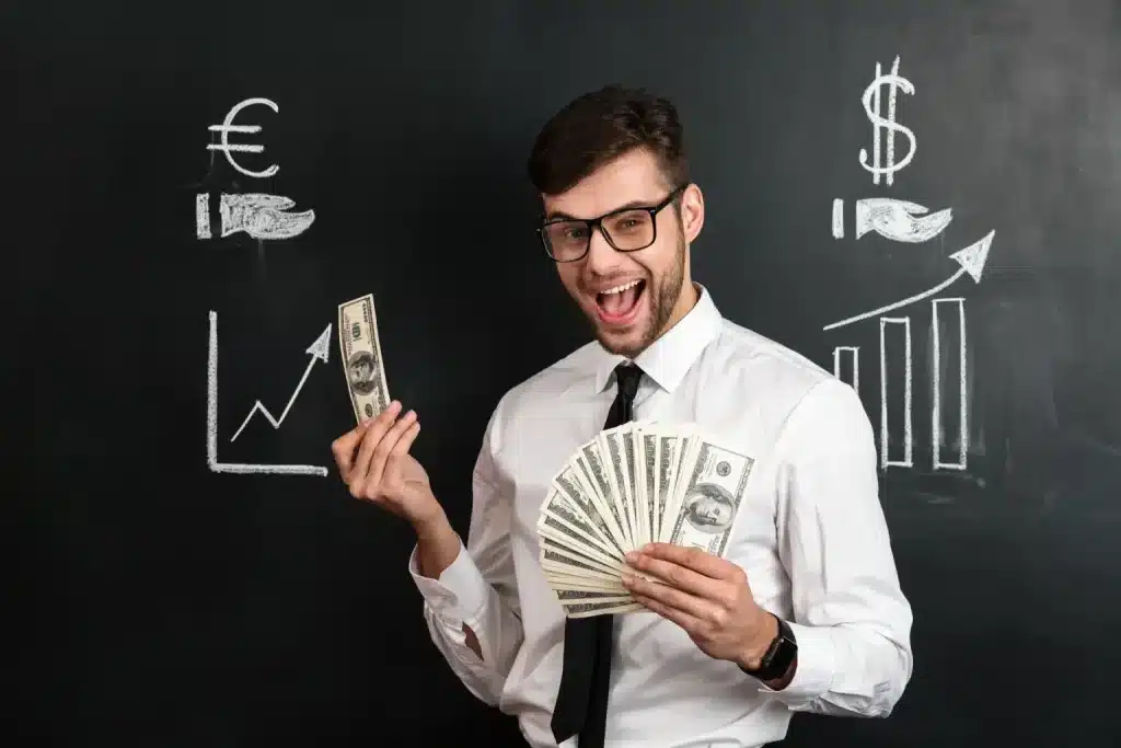 Executivo segurando notas de dólar diante de quadro com gráficos de alta e símbolos de moedas, representando profissões com salários de até R$ 100 mil mensais.