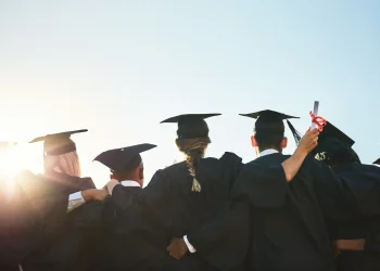 Grupo de formandos comemorando a graduação ao ar livre, simbolizando o momento de transição entre a conquista acadêmica e as dificuldades profissionais.