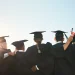 Grupo de formandos comemorando a graduação ao ar livre, simbolizando o momento de transição entre a conquista acadêmica e as dificuldades profissionais.