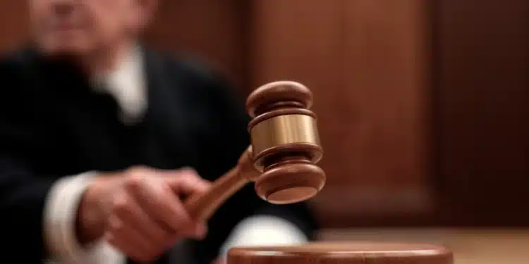 Mão de juiz bate martelo na mesa em tribunal de madeira