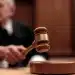 Mão de juiz bate martelo na mesa em tribunal de madeira