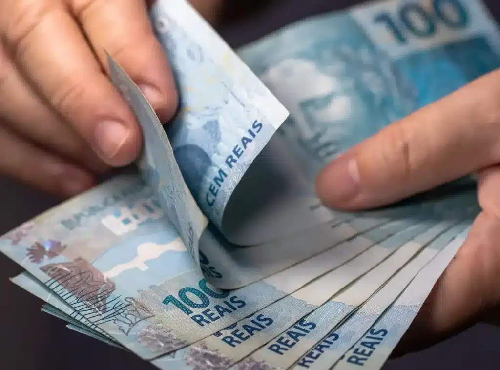 Trabalhador segurando notas de cem reais relacionadas ao Saque Calamidade do FGTS após desastre natural.