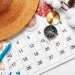 Calendário com chapéu de verão, bússola e miniatura de avião representando planejamento do feriado da Sexta-feira da Paixão 2026.