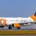 Aeronave Boeing 737 da GOL Linhas Aéreas taxiando em uma pista de aeroporto sob o sol. O avião possui a fuselagem branca com o logotipo laranja e uma pintura especial na cauda celebrando 150 anos com a imagem de Santos Dumont.