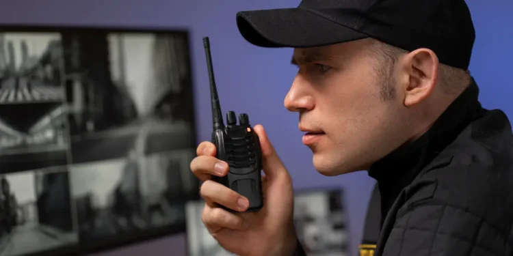 Vigilante utiliza rádio comunicador diante de monitores de segurança.