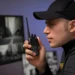 Vigilante utiliza rádio comunicador diante de monitores de segurança.