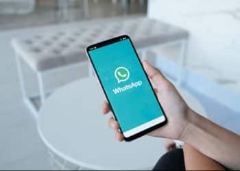 Pessoa segurando um smartphone com a tela do WhatsApp visível, mostrando o ícone do aplicativo em um ambiente moderno e claro.