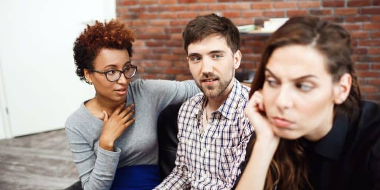 Três pessoas amigas sentadas em uma cafeteria, uma delas demonstra chateação com os outros amigos.