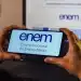 Pessoa segurando celular com a Página do Participante do Enem aberta enquanto acessa o sistema pelo notebook.
