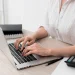 Mulher utilizando notebook ao lado de calculadora para verificar débitos e pendências fiscais com a nova ferramenta digital da Receita Federal.