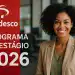 Jovem profissional sorrindo em escritório ao lado de painel vermelho do Programa de Estágio Bradesco 2026.