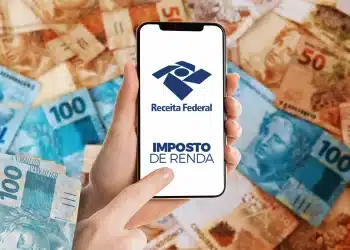 Pessoa acessando aplicativo da Receita Federal com cédulas de real ao fundo.