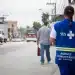 Profissional do SUS caminha em rua de bairro enquanto segura papéis, usando colete azul