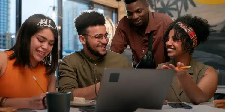 Quatro colegas de trabalho sorrindo e se comunicando durante uma reunião, demonstrando um ambiente de amizade e colaboração no escritório.