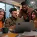 Quatro colegas de trabalho sorrindo e se comunicando durante uma reunião, demonstrando um ambiente de amizade e colaboração no escritório.
