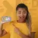 Jovem estudante empolgada apontando para o aplicativo do Pé-de-Meia no celular, representando a necessidade de atualizar o CadÚnico para garantir o benefício