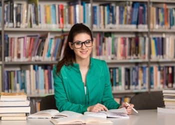 Profissional de Biblioteconomia consultando livros em biblioteca e trabalhando com organização do conhecimento.
