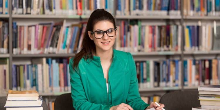 Profissional de Biblioteconomia consultando livros em biblioteca e trabalhando com organização do conhecimento.