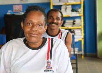 Estudantes adultos com uniforme da Prefeitura de Alagoinhas sorrindo em sala de aula, beneficiários do programa Bolsa Presença de R$ 100 mensais