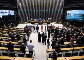 Vista panorâmica do plenário da Câmara dos Deputados em Brasília, com parlamentares ocupando as bancadas e grandes telas de votação exibindo informações sobre os projetos em pauta.
