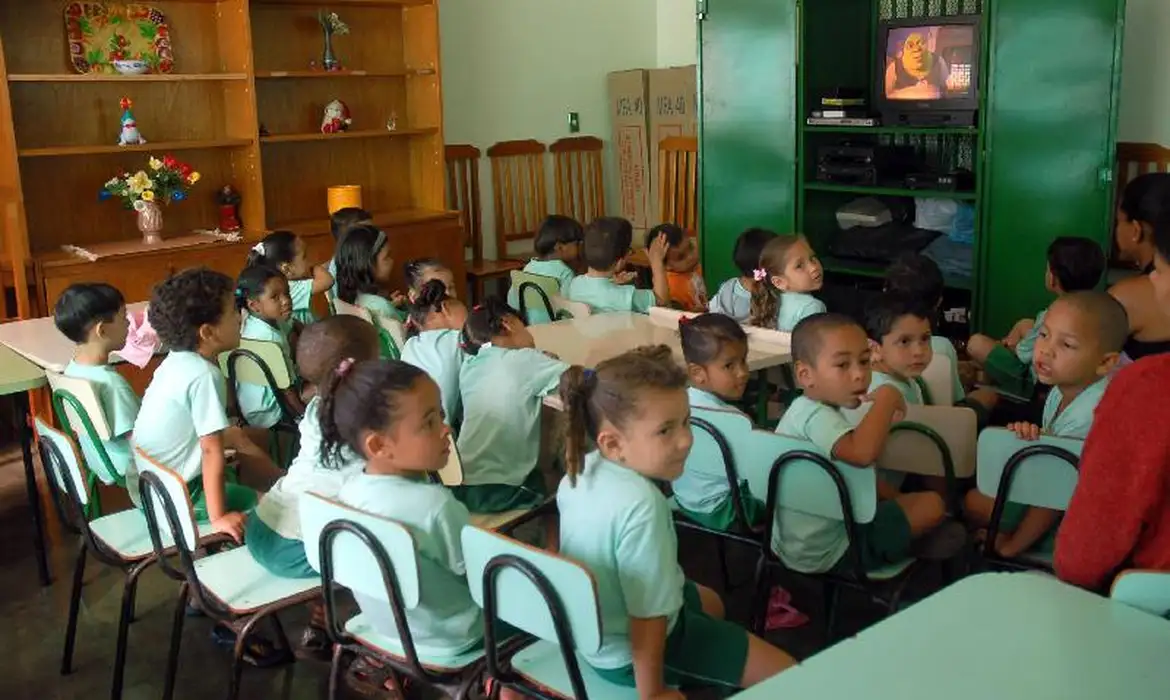 Crianças pequenas uniformizadas sentadas em sala de aula, representando a primeira infância em situação de vulnerabilidade social atendida pelo Cartão da Primeira Infância Carioca, benefício de R$ 200 mensais da Prefeitura do Rio de Janeiro