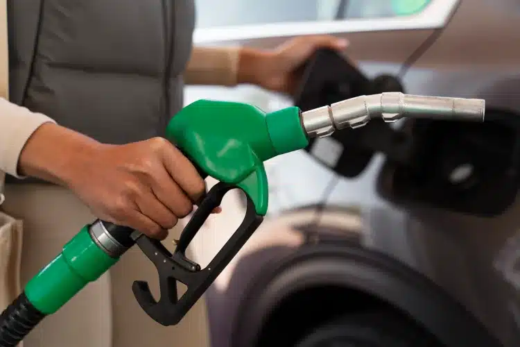 Mão segura bomba de combustível verde enquanto abastece carro em posto