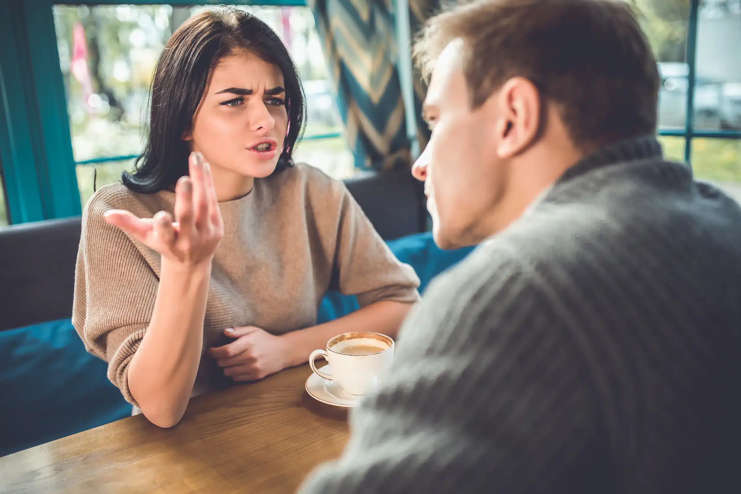 Mulher gesticulando com irritação e expressão de julgamento enquanto confronta um homem em um café, ilustrando falhas na inteligência emocional e comunicação agressiva.