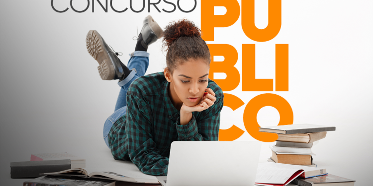 Jovem deitada usando notebook cercada de livros estudando para concurso público