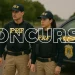 Dois agentes da Polícia Rodoviária Federal uniformizados posicionados ao lado de viatura oficial da PRF