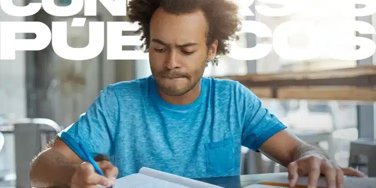 Homem jovem de camiseta azul e cabelo afro, concentrado ao escrever em um caderno enquanto estuda com livros abertos. Ao fundo, o texto "CONCURSOS PÚBLICOS" em letras brancas vazadas.