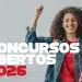 Jovem estudante sorrindo com o punho erguido em sinal de comemoração, segurando livros e mochila, representando a oportunidade de ingressar no serviço público por meio do concurso da Secretaria Municipal de Educação com 471 vagas abertas em 2026