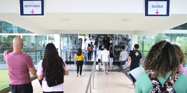 Candidatos entrando em local de prova com placas de entrada e saída visíveis representando o dia de aplicação das provas do concurso do IBGE 2026