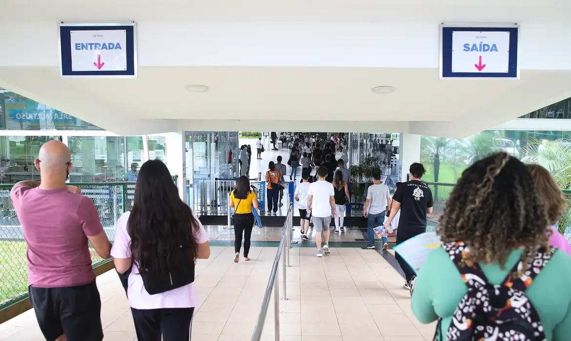 Candidatos entrando em local de prova com placas de entrada e saída visíveis representando o dia de aplicação das provas do concurso do IBGE 2026