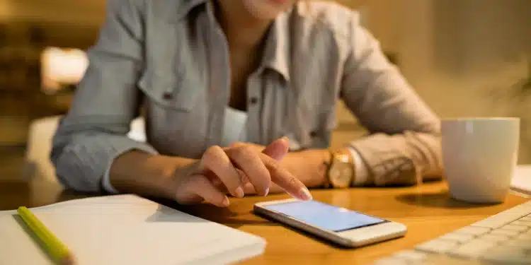 ulher sorrindo toca a tela do celular enquanto prepara currículo ao lado de caderno