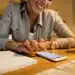 ulher sorrindo toca a tela do celular enquanto prepara currículo ao lado de caderno