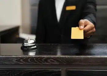 Funcionário de recepção entrega cartão amarelo sobre balcão ao lado de campainha