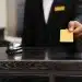 Funcionário de recepção entrega cartão amarelo sobre balcão ao lado de campainha