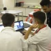 Dois jovens estagiários trabalhando em laptops em uma sala, com um supervisor de jaleco branco orientando, representando o ambiente de estágio profissional e os direitos trabalhistas propostos pelo PL 6350/25.