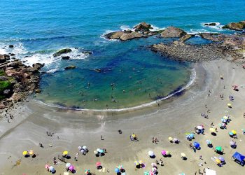 Pessoas aproveitando praia com guarda-sóis coloridos e mar calmo na cidade litorânea