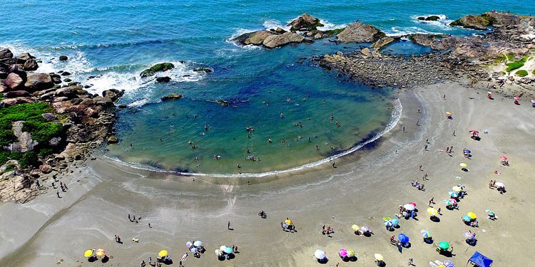 Pessoas aproveitando praia com guarda-sóis coloridos e mar calmo na cidade litorânea